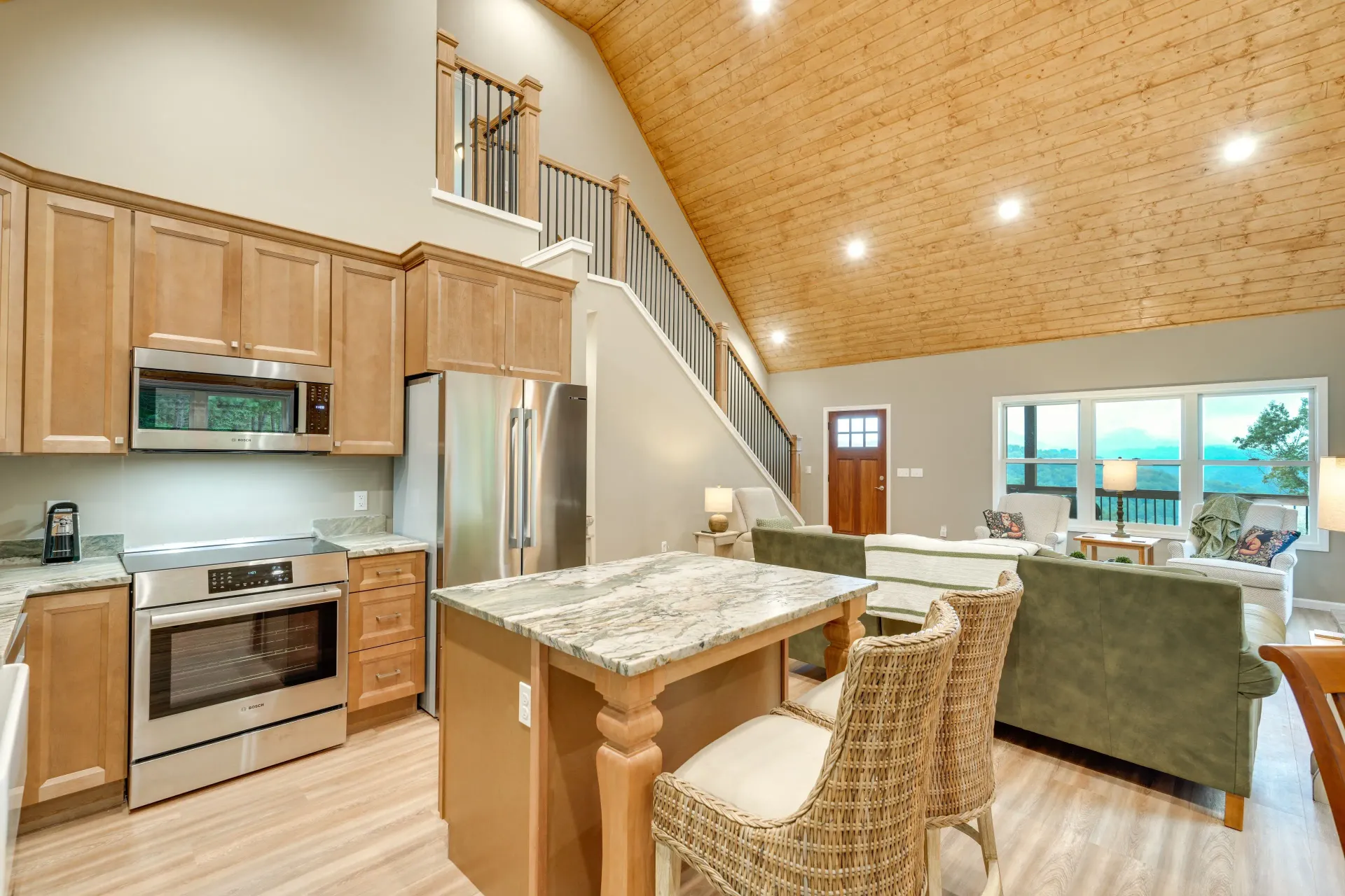 Open kitchen and living room with granite island, wood cabinets, vaulted ceiling, and green sofa.