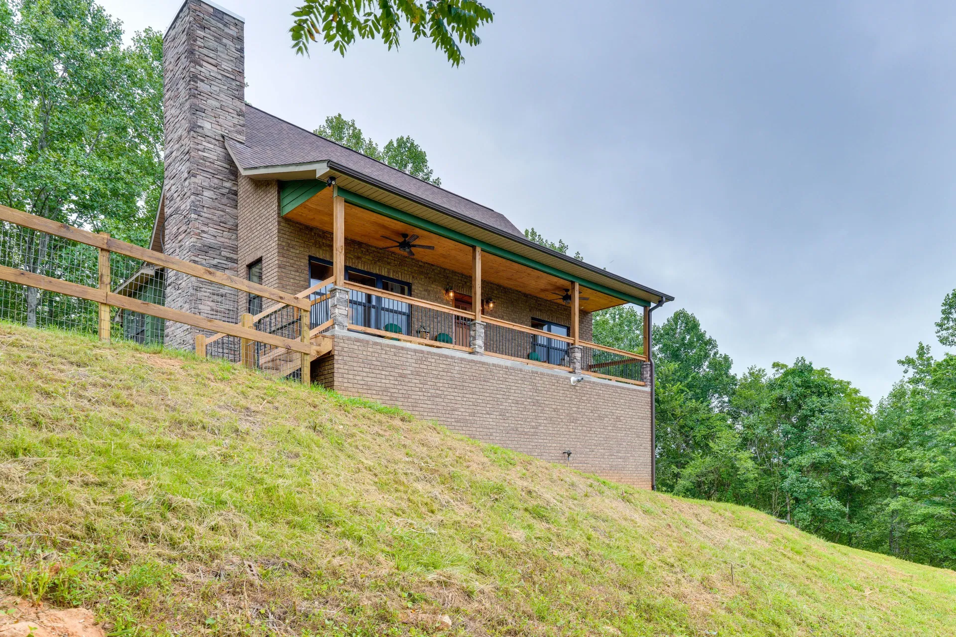 Stone cabin with a covered porch on a grassy hillside under a cloudy sky