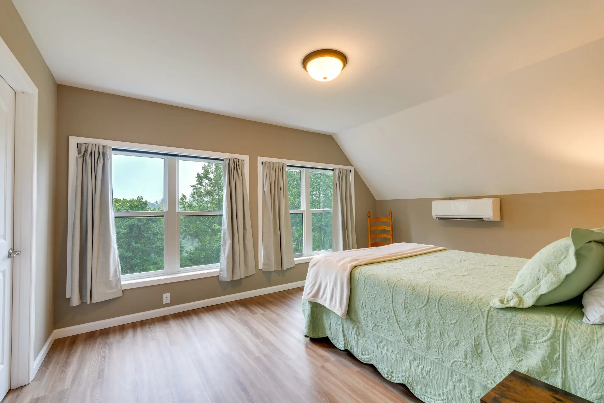Bright bedroom with large windows, wood flooring, and a bed with mint green bedding