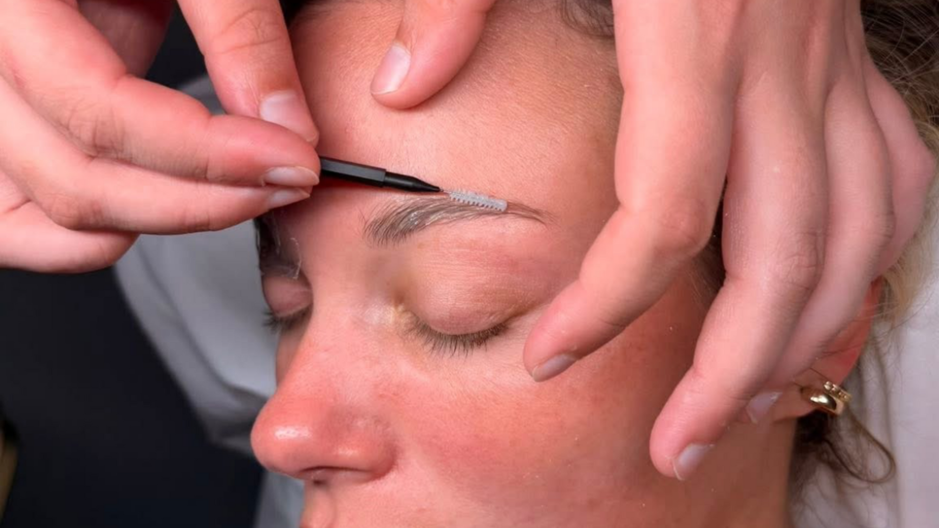 Hands shaping a woman’s eyebrow with a brow tool, close-up on her face