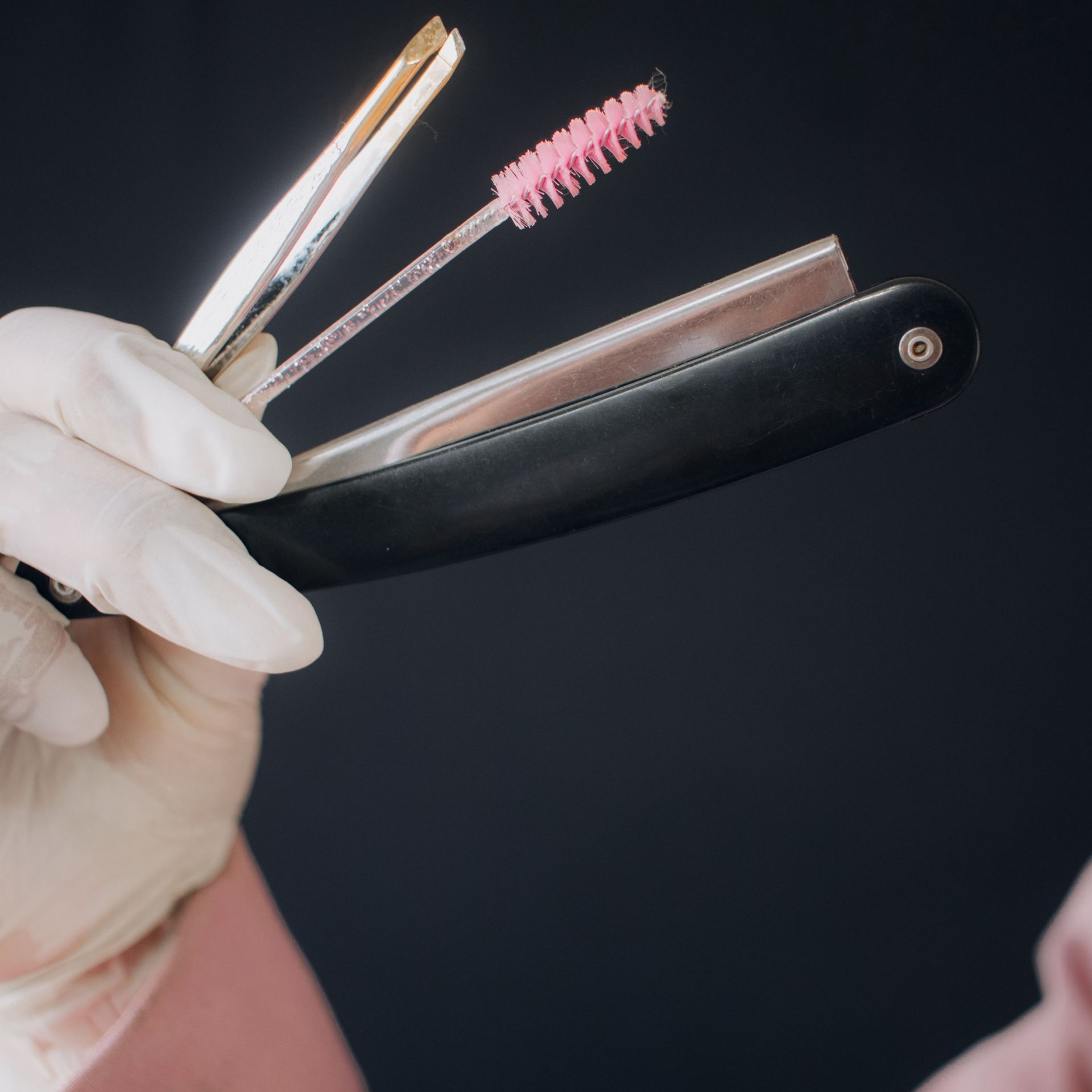 Gloved hand holding a blade with a pink cleaning brush on a dark background