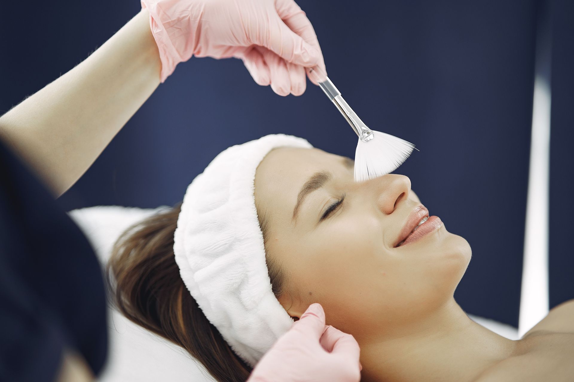 Spa treatment: a woman receives a facial with a brush while lying back with a white headband