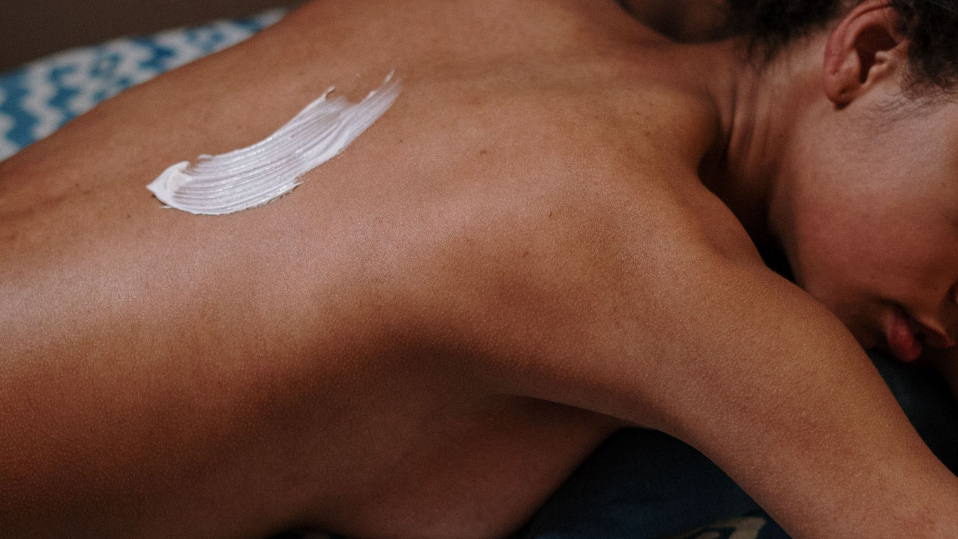Person receiving a white cream massage on upper back and shoulder