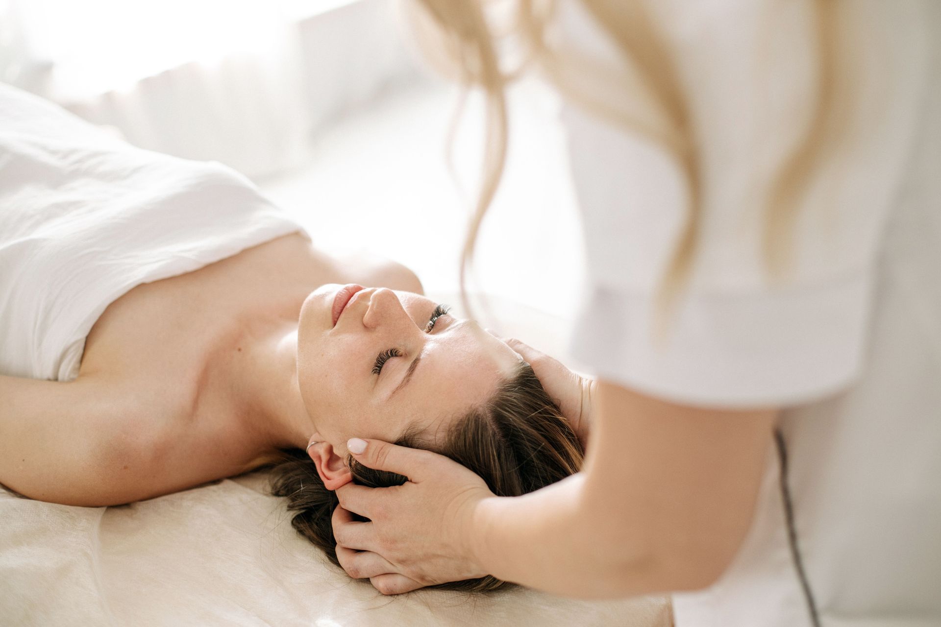 A massage therapist gently massages a client’s temples as the client lies face down on a table.