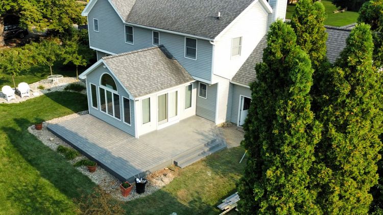 Aerial view of a white house with a patio, surrounded by green lawn and tall trees.