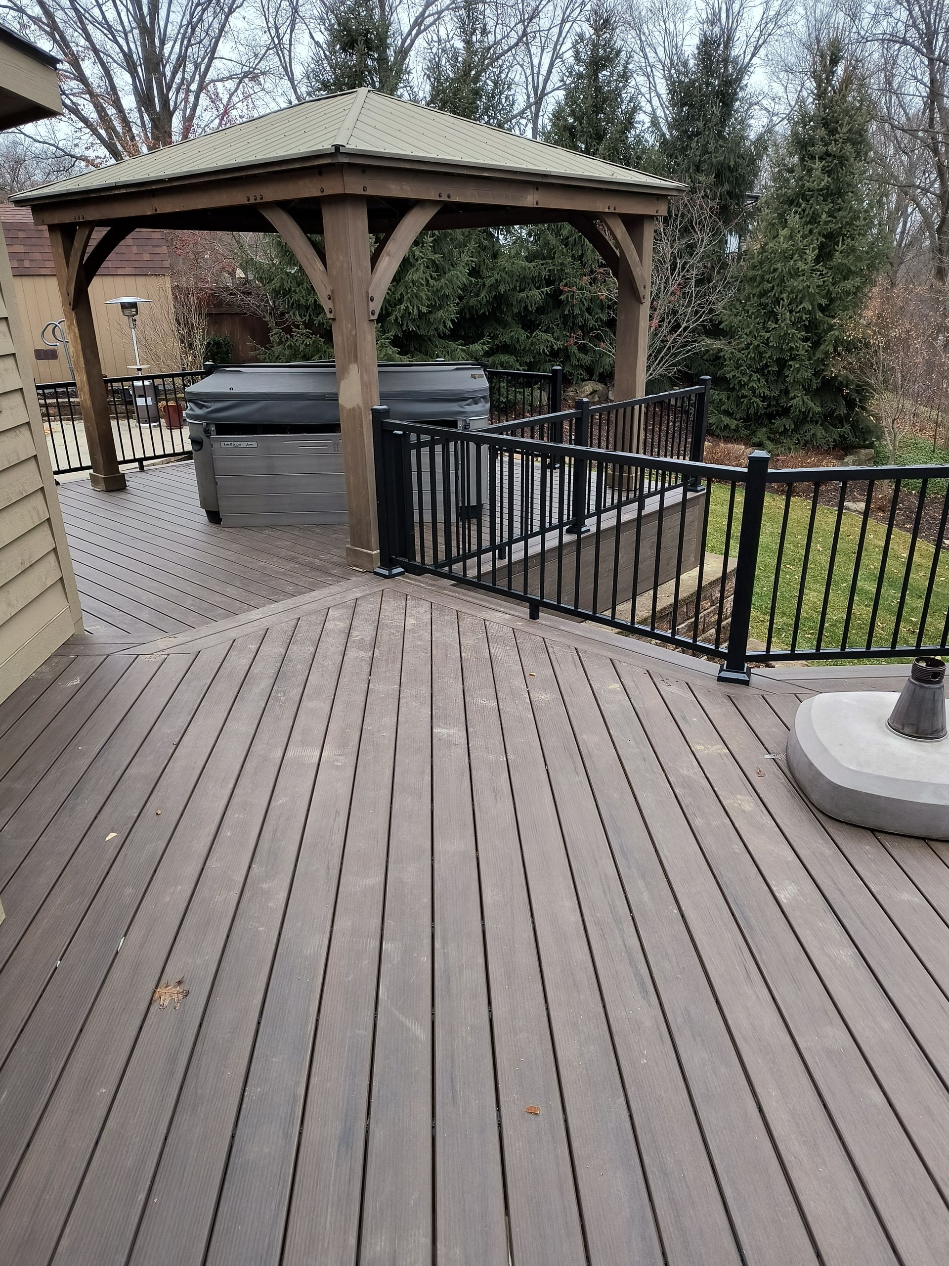 Wooden deck leading to a gazebo with a hot tub, black railing, and a small lawn in the backyard.