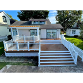 White house with a large front porch, deck, and steps in a sunny suburban yard