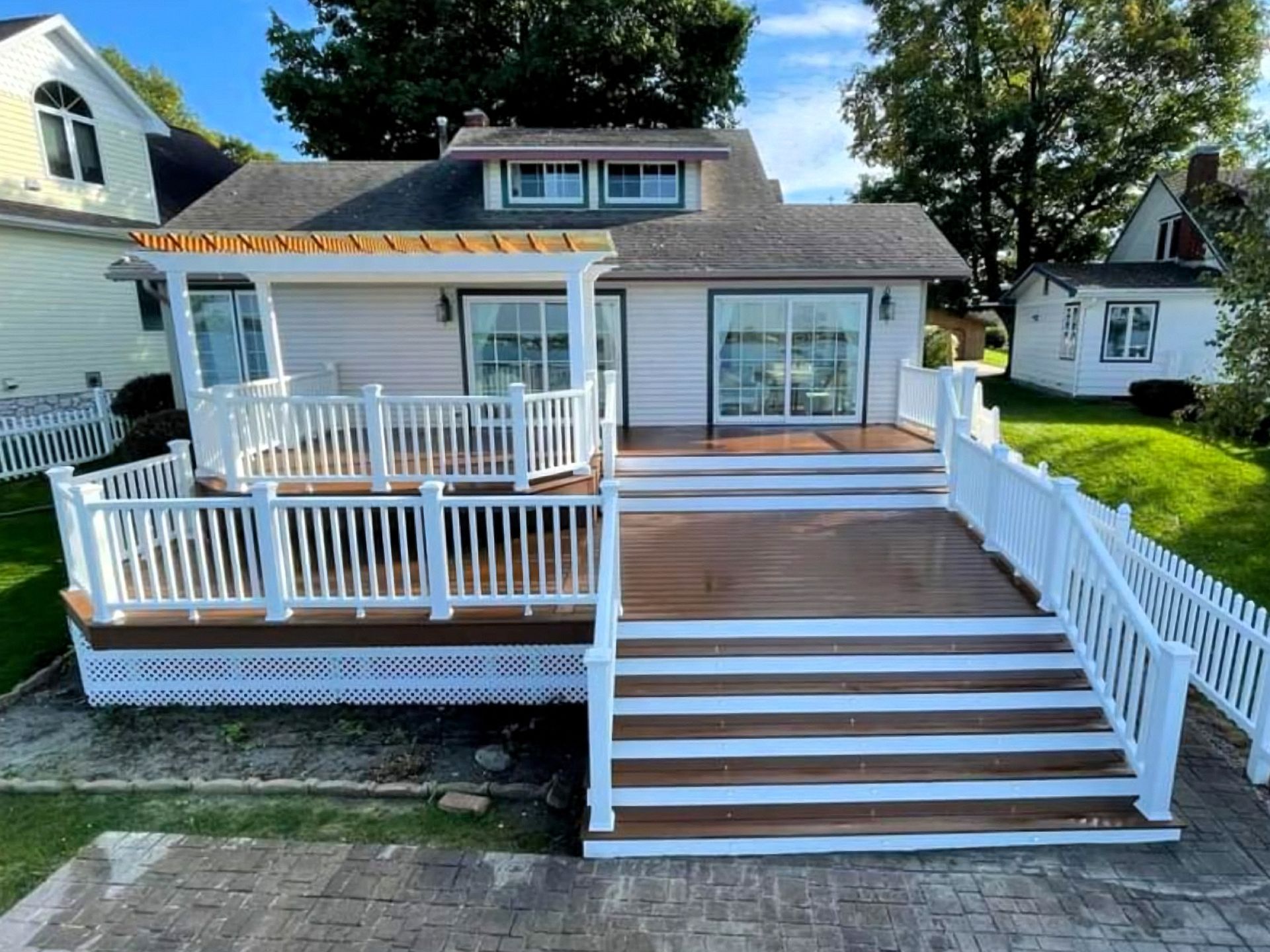 White house with a large front porch, deck, and steps in a sunny suburban yard
