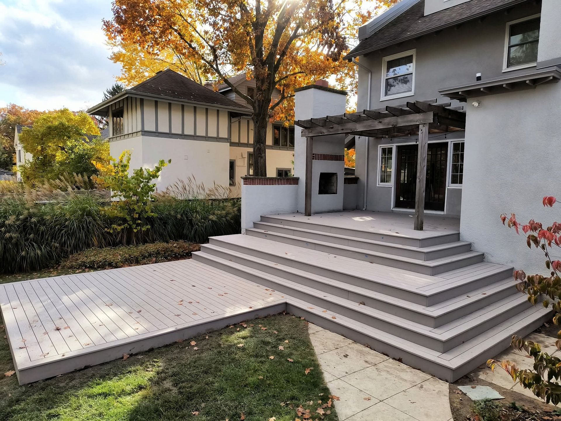 Modern house patio with wide gray steps, tiled terrace, and autumn trees in the background