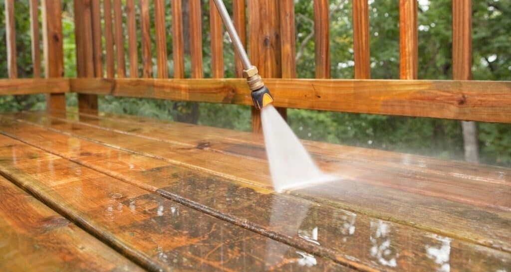 Pressure-washing a wet wooden deck with a spray nozzle beside a railing