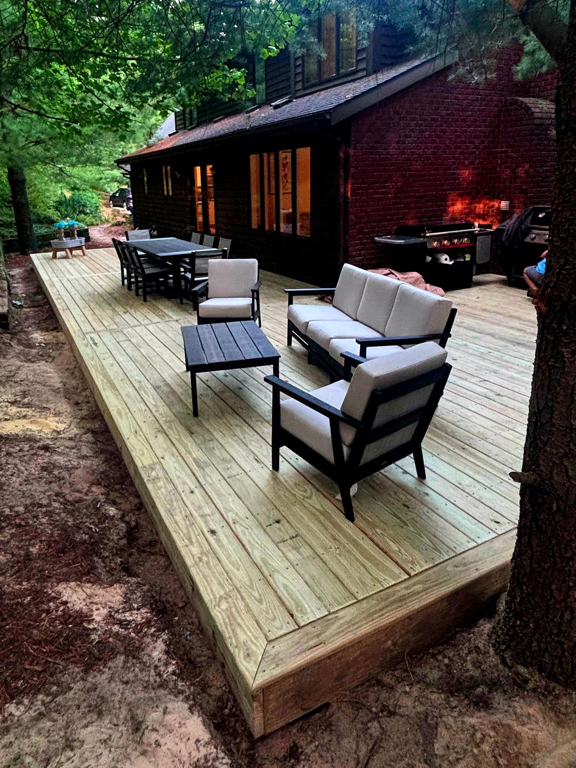 Wooden deck with black patio furniture beside a rustic cabin in a wooded setting.