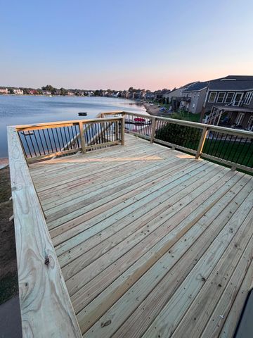 Wooden deck overlooking a calm bay at sunset, with railings and waterfront homes in the distance
