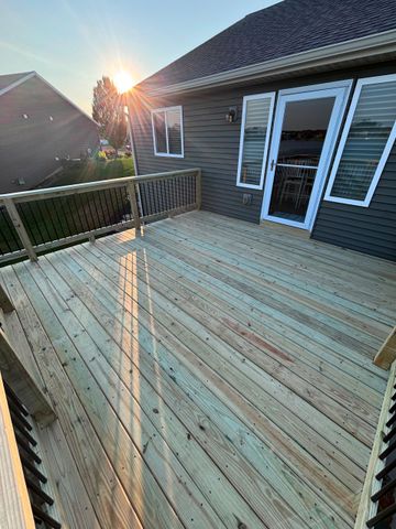 Wooden backyard deck beside a house at sunset, with railing and open French doors