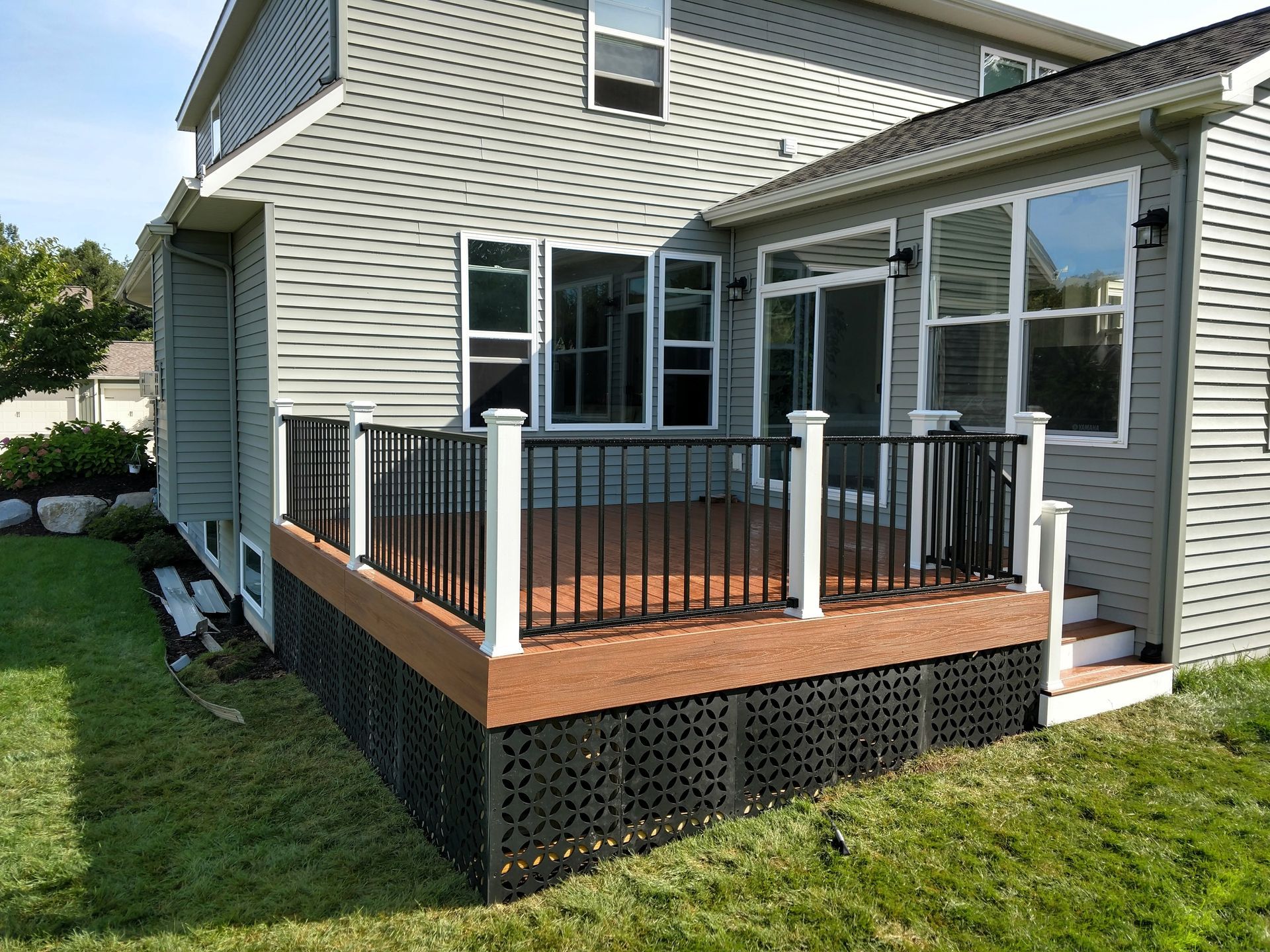 Back deck with wooden floor, black railings, and white posts on a beige house exterior