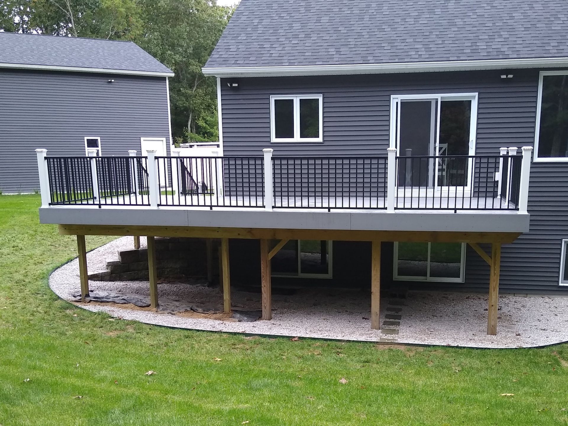 Raised deck on a gray house with black railing and white-trimmed sliding doors in a grassy yard.