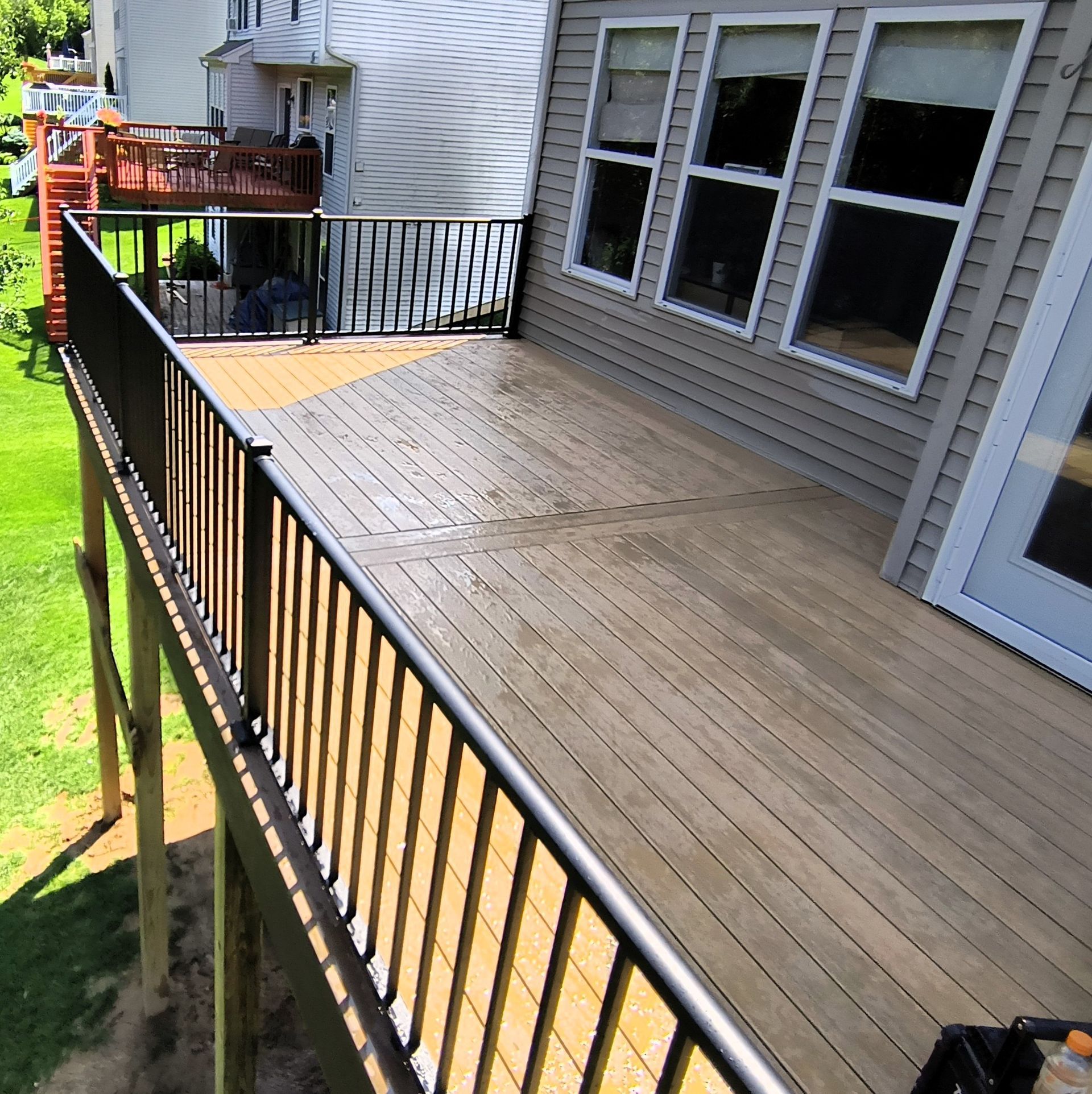 Wooden backyard deck with black railings beside a house and a lawn below