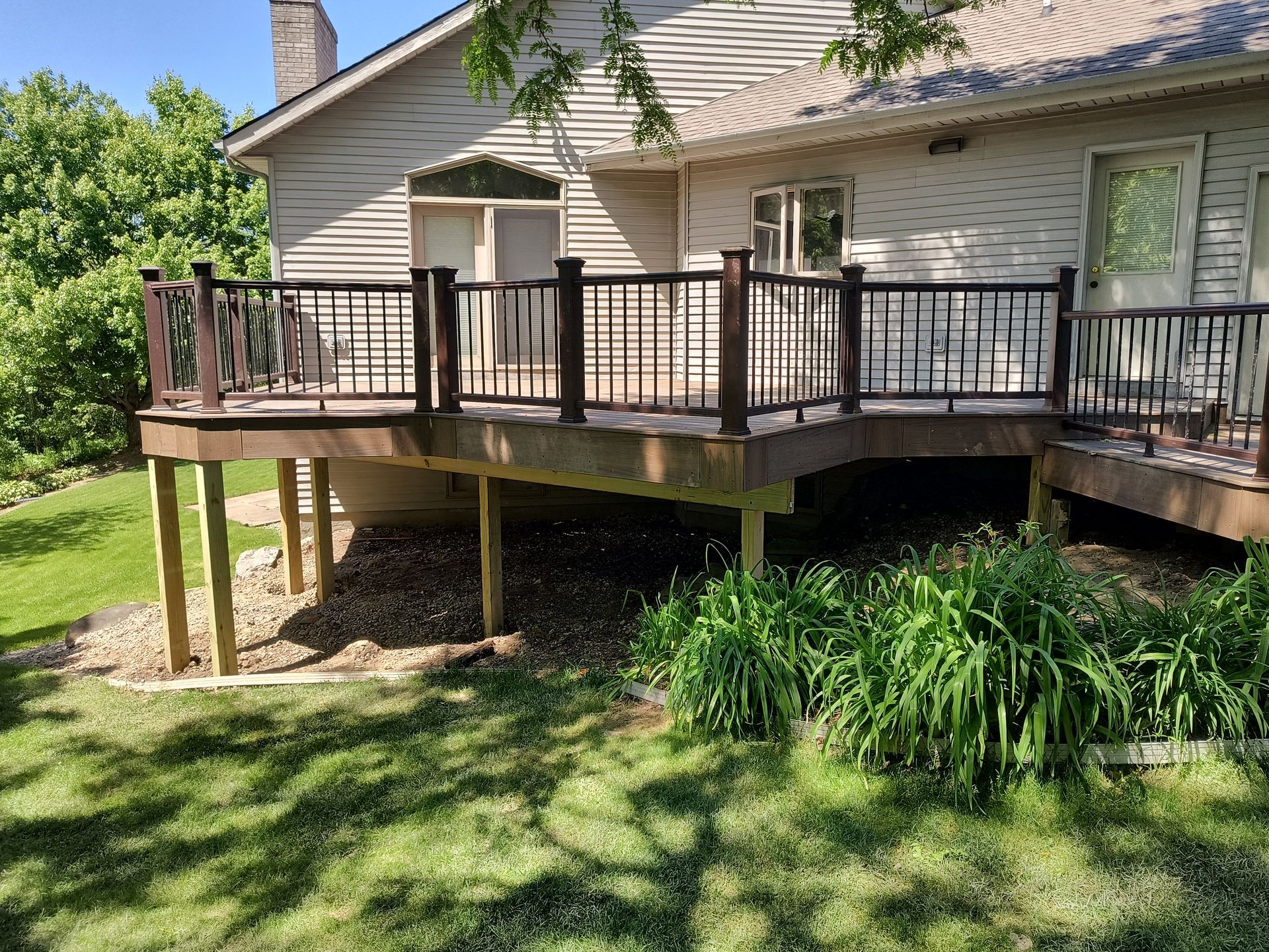Back deck with wooden railing on a beige house, overlooking a grassy yard and garden plants