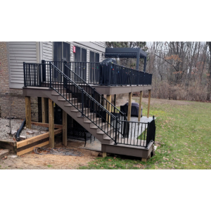 Raised backyard deck with black railings and stairs leading down to a grassy yard