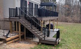 Backyard deck with black stairs and railing attached to a house, overlooking a grassy yard.