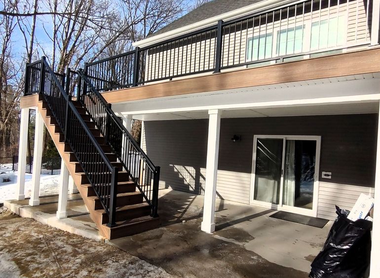 Exterior of a building with an outdoor staircase, balcony, and sliding glass doors on a sunny day