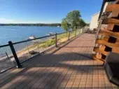 Lakeside wooden deck with black railings beside calm water on a sunny day