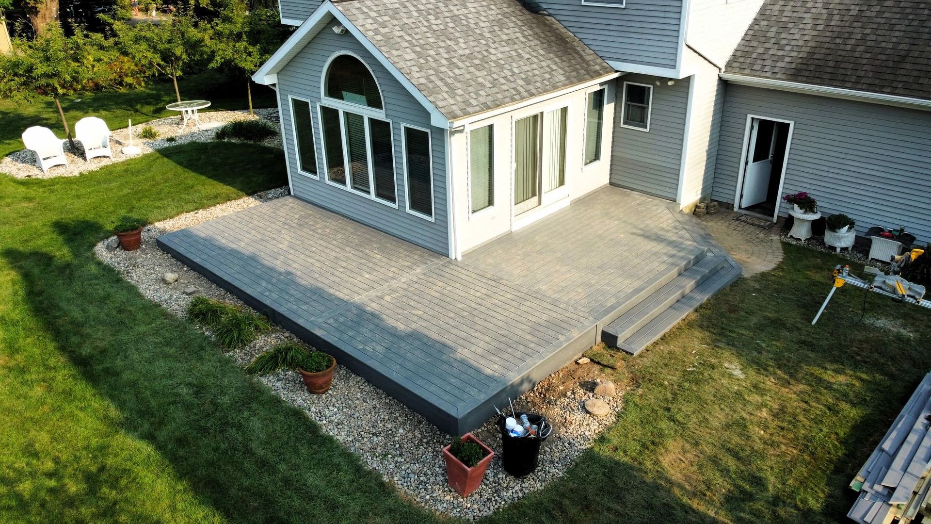 Backyard patio with large screened sunroom, gray pavers, and steps beside a house in a grassy yard