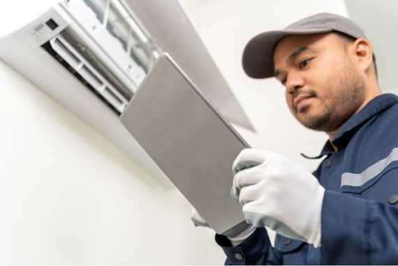 A man is working on an air conditioner while looking at a tablet.