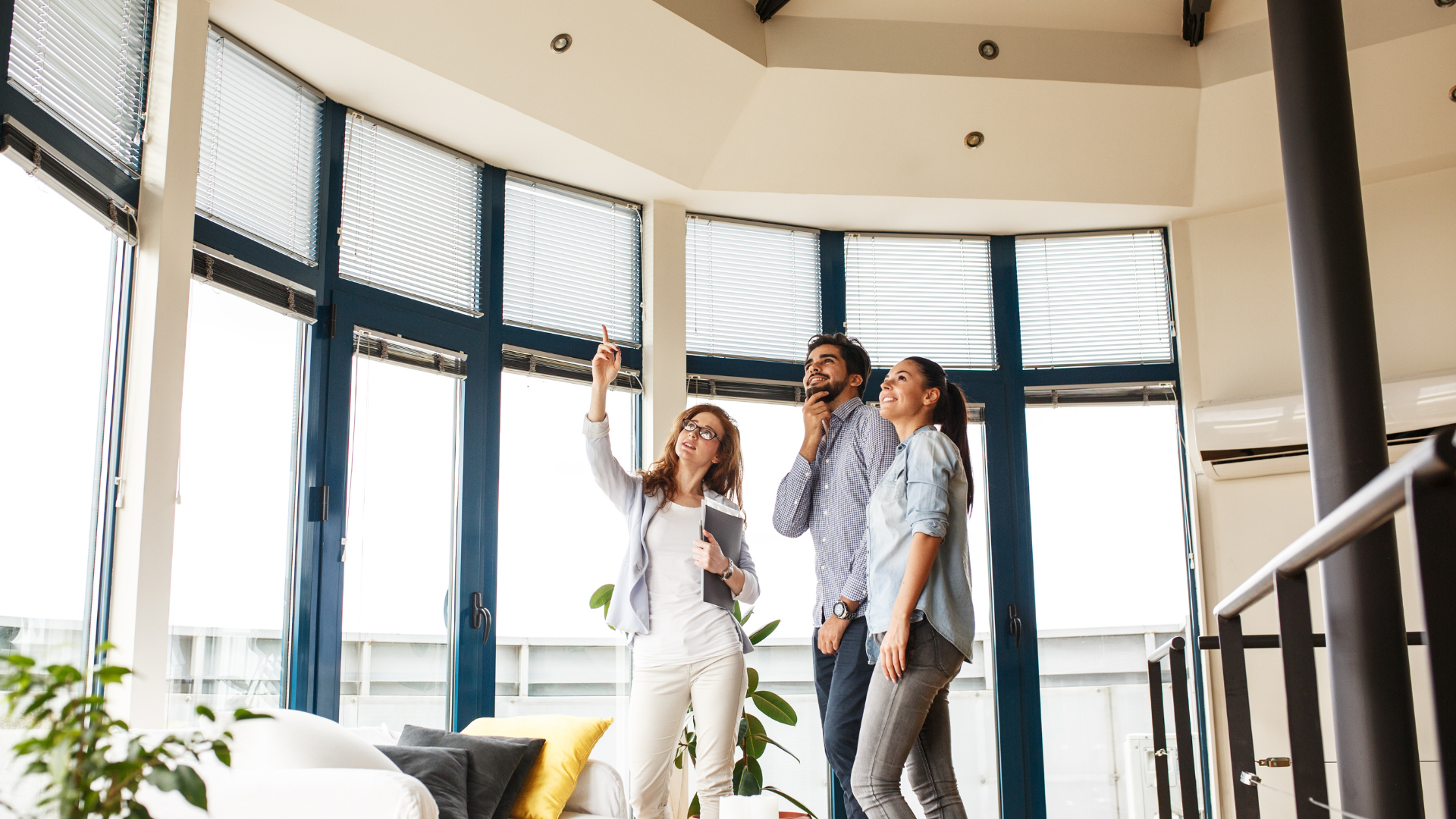 Three people standing in a bright room, pointing up at the window blinds.