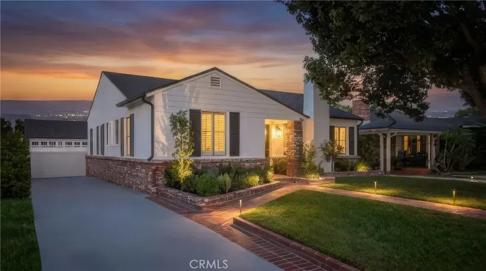 Single-story suburban house at dusk with warm lights, stone accents, and a driveway by a green lawn