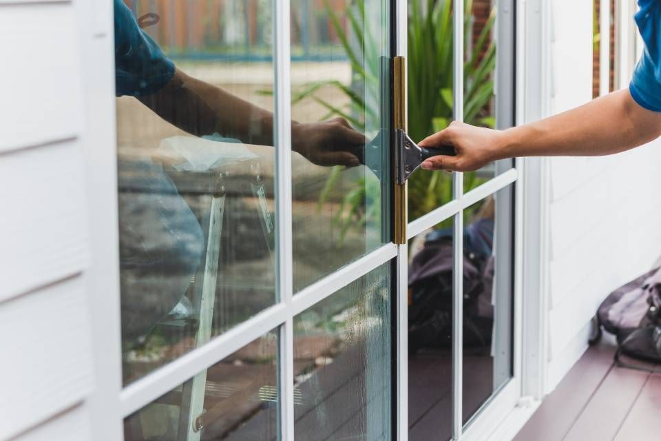 A person in a blue shirt opening a white-framed glass sliding door on a wooden deck.