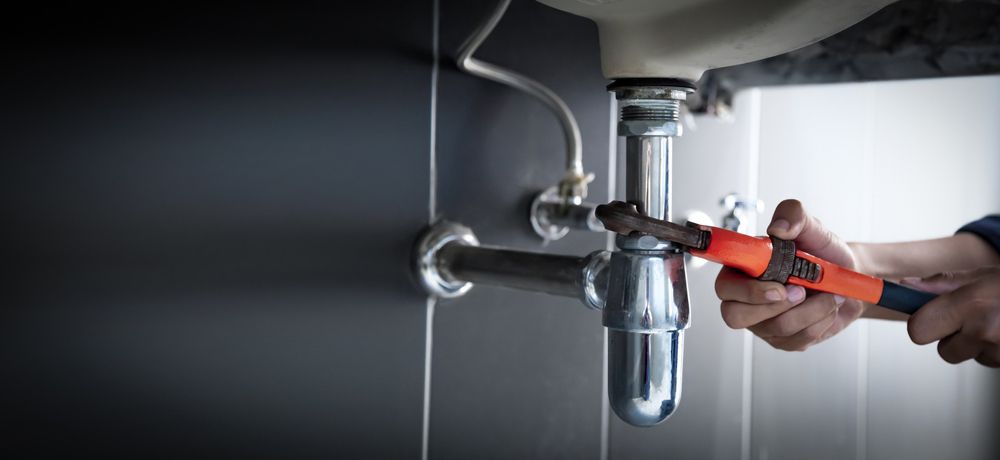 A Person Using a Wrench to Repair a Chrome Plumbing Pipe Under a Sink — FNQ Footprints Plumbing In Whitfield, QLD