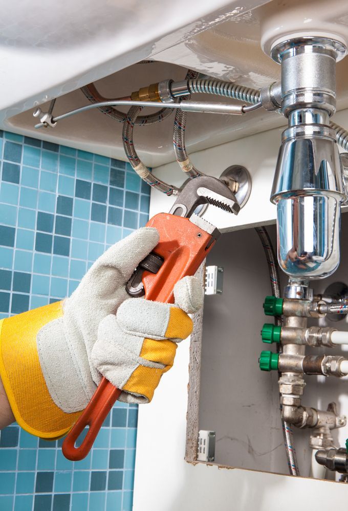 Plumber in Yellow Work Gloves Using an Adjustable Wrench Under a Sink — FNQ Footprints Plumbing In Whitfield, QLD