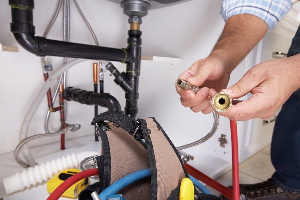 Plumber Working Under a Kitchen Sink, Holding a Fitting — FNQ Footprints Plumbing In Whitfield, QLD