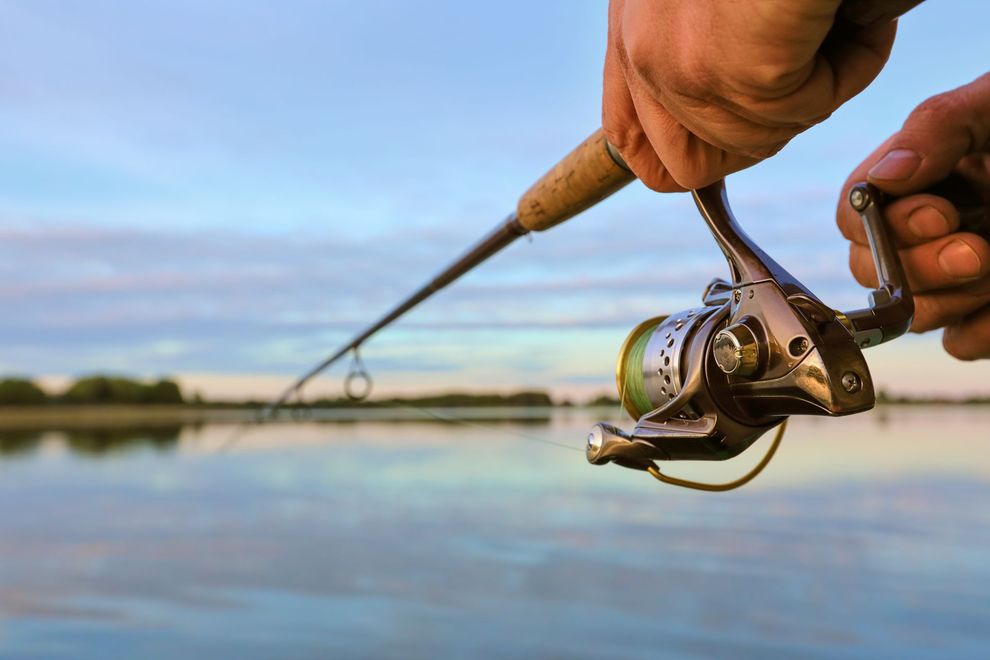 Hands holding a fishing rod and reel over calm water at sunset