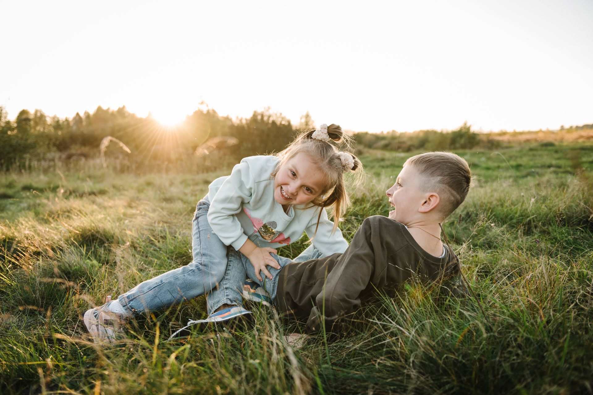 Two children laughing in a grassy field at sunset