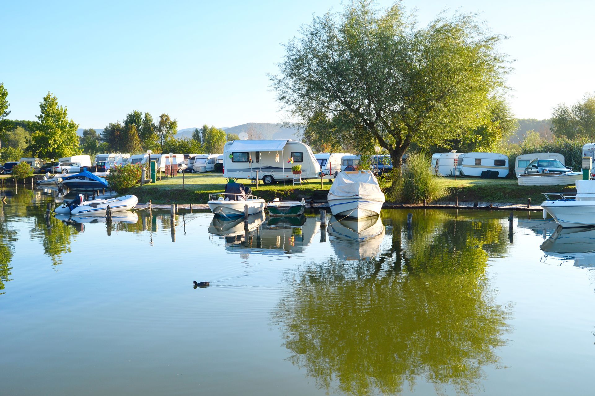 Marina with boats and RVs beside a calm lake, reflecting trees and a blue sky