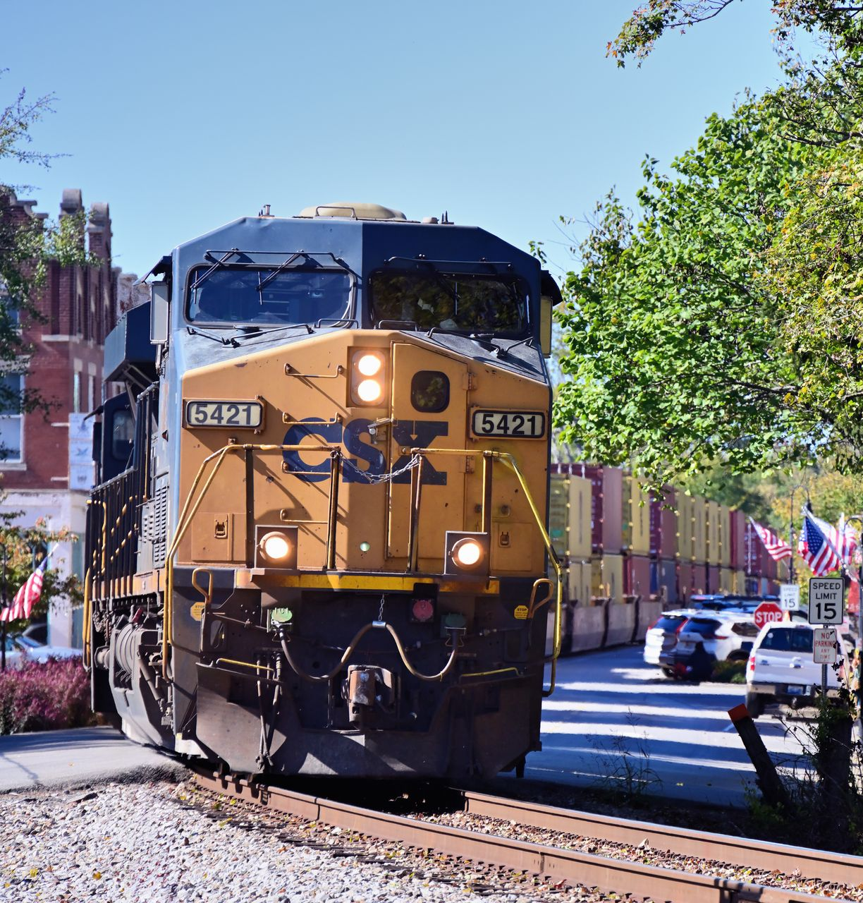 Yellow freight locomotive rounding a curve on tracks in a sunny urban street