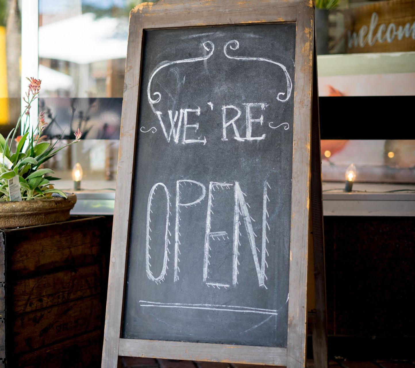 Chalkboard sign at a storefront reads “WE’RE OPEN” in white chalk.