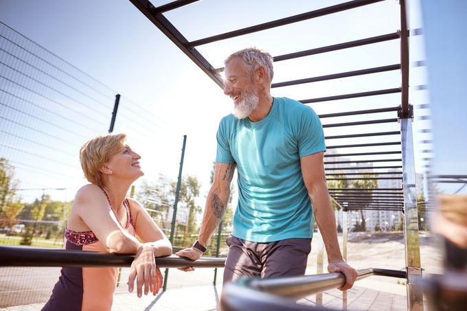 Smiling older couple looking at a tablet together outdoors. Woman has her arms around the man, who is holding the device.