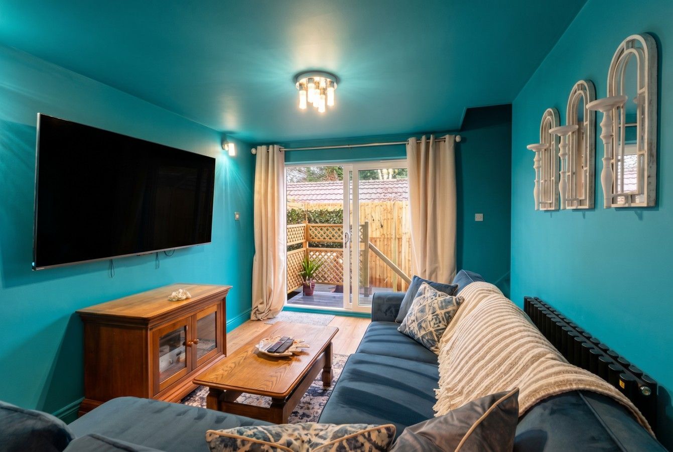 Turquoise living room with wall-mounted TV, sofa, coffee table, and sliding doors to a balcony.