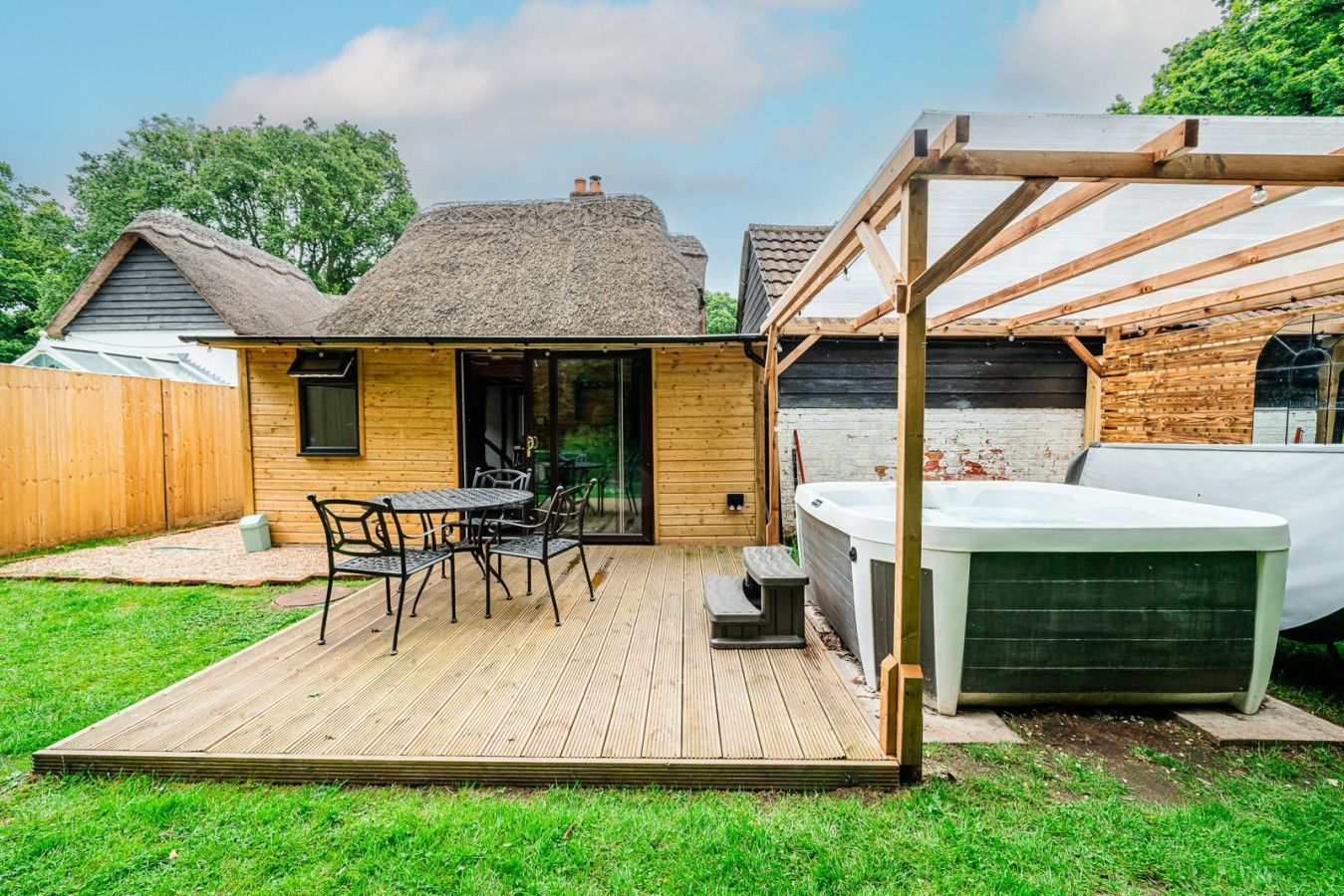 Backyard patio with wooden deck, small cabin, outdoor dining set, and hot tub under a pergola
