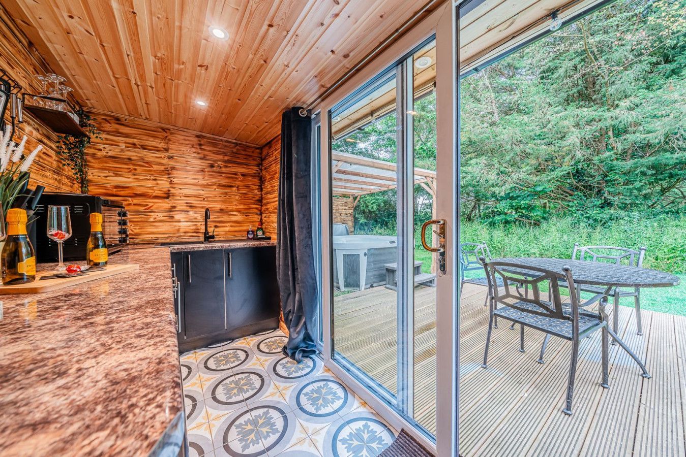 Wood-paneled sunroom with a grill and table beside sliding glass doors to a deck and forest view