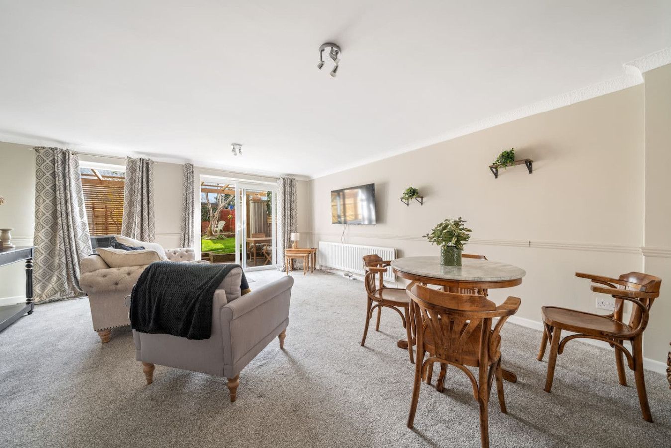 Bright living-dining room with gray sofa, round wooden table, large windows, and beige walls