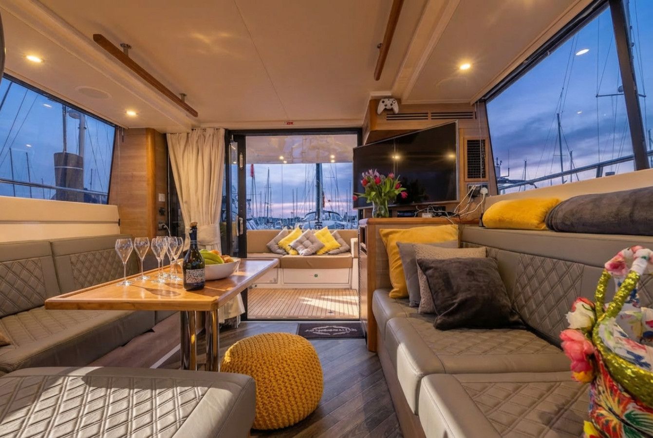Cozy luxury lounge with sofa seating, table, flowers, and large windows overlooking a sunset harbor.