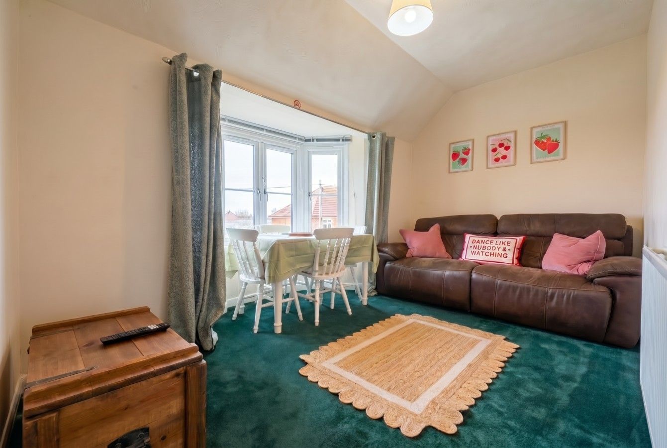 Cozy living room with brown sofa, teal carpet, small dining table, and bay window with curtains