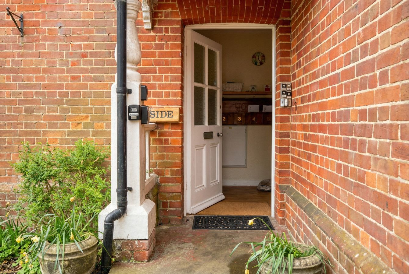 Brick front entrance with open white door, wet steps, and potted plants by the doorway