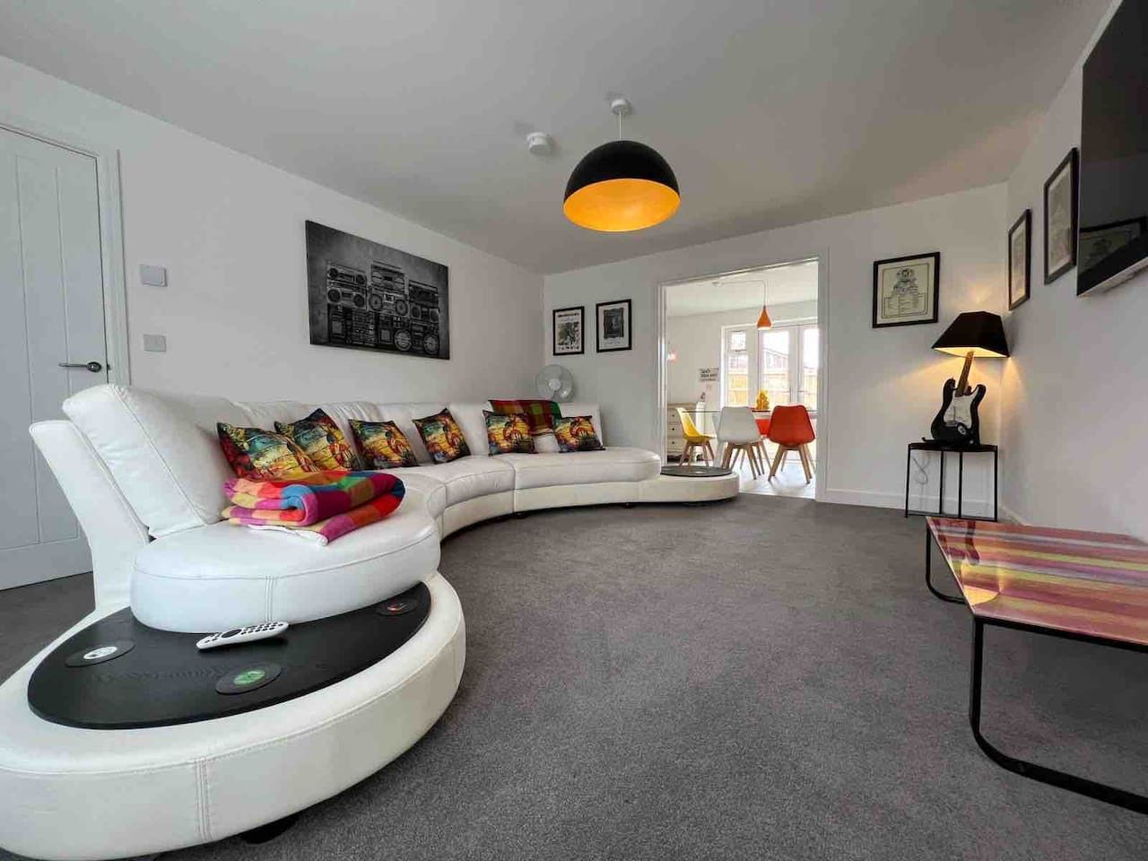 Modern living room with curved white sofa, colorful pillows, and gray carpet under a black pendant light