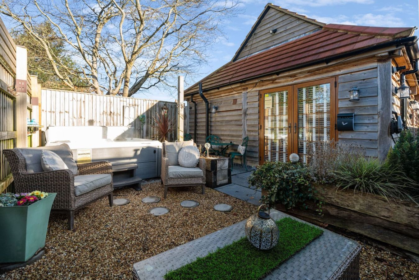 Backyard patio with wicker seating, gravel path, potted plants, and a small wooden shed under a sunny sky
