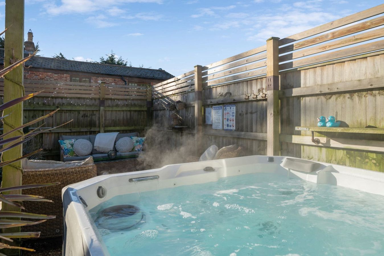 Backyard hot tub with steaming water beside a fenced patio and blue sky