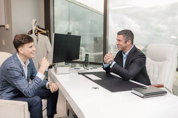 A man is sitting at a desk talking to another man.